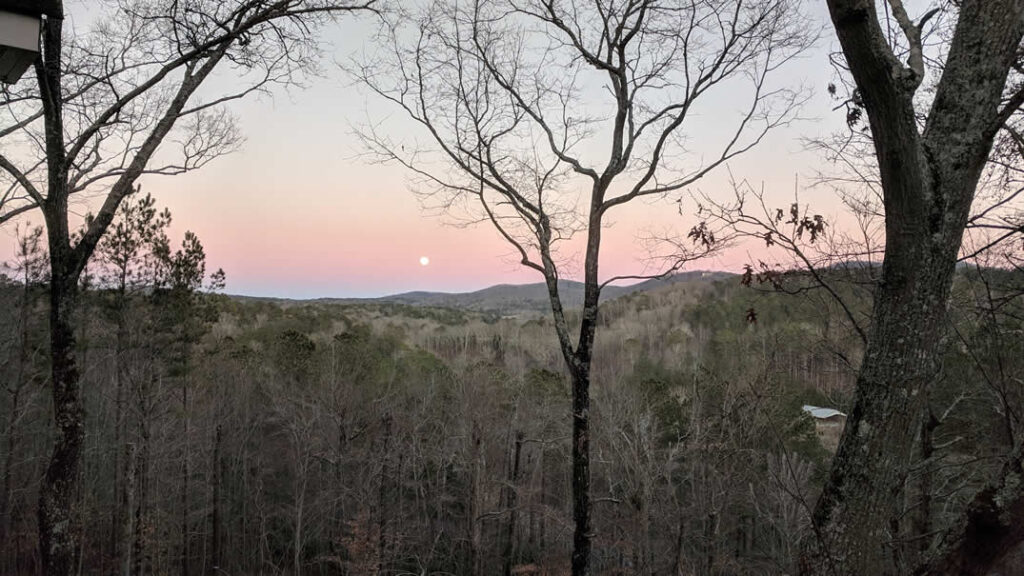 Sunset over forested hills with visible moon
